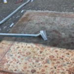 This is a photo of a floral rug that is being steam cleaned. The bottom half has been completed and the top half is being done carried out by Purley Carpet Cleaning Solutions.