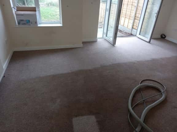 This is a photo of an empty living room with a brown carpet that is in the process of having its carpets steam cleaned carried out by Purley Carpet Cleaning Solutions.