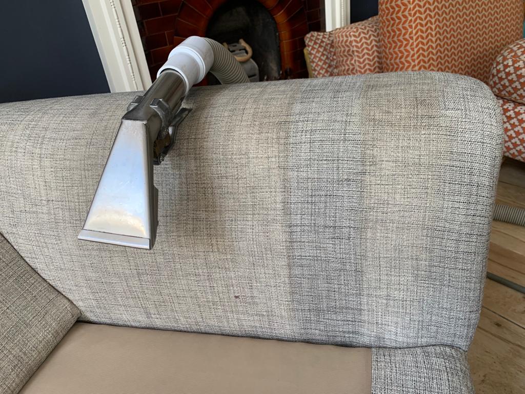 This is a photo of an arm of beige sofa that shows a test patch that has been steam cleaned. The steam cleaning machine is also showing in the photo works carried out by Purley Carpet Cleaning Solutions.