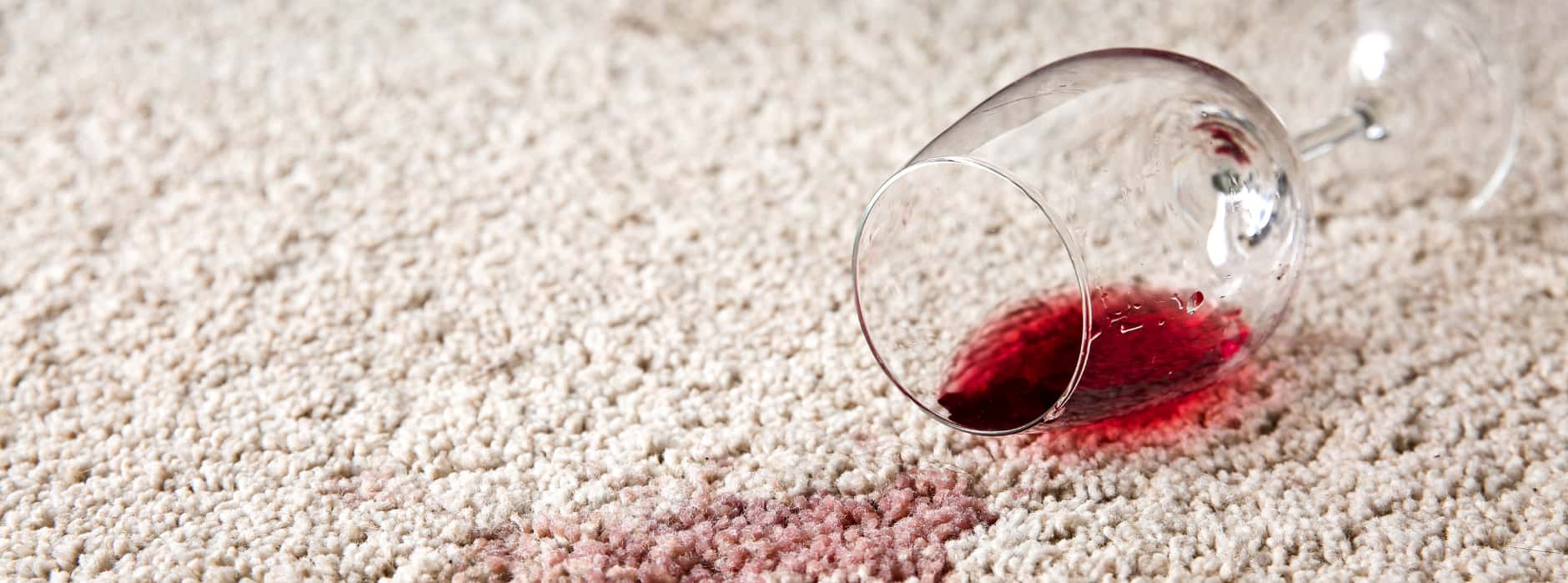 This is a photo of  red wine which has been spilt on a cream carpet. The glass is on its side.